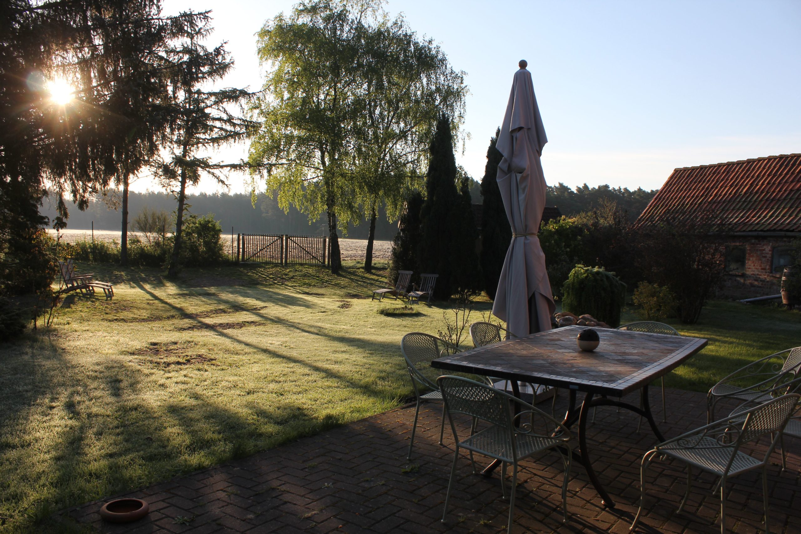 Foto zeigt Terasse mit Tisch, Sonnenschirm und die Weite des Gartens
